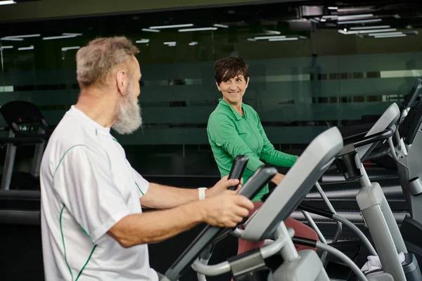 Femme gaie regardant homme âgé, mari et femme travaillant dans la salle de gym, personnes âgées actives, sport — Photo de stock