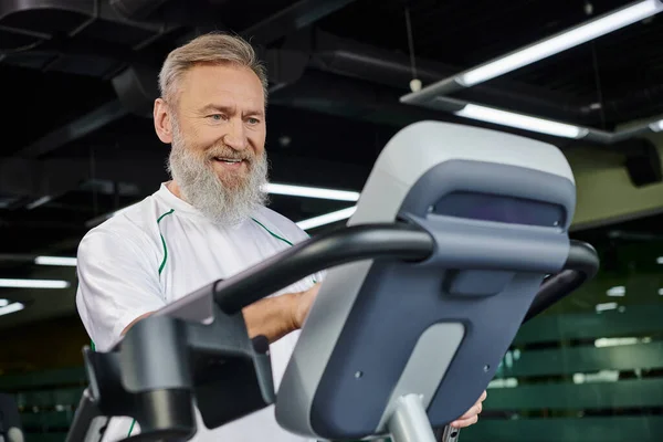Счастливый и бородатый мужчина упражнения на беговой дорожке, кардио, спорт, пожилые тренировки, активный старший — стоковое фото