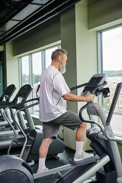 Bearded senior man working out on stepper exercise machine, elderly in gym, active senior, sport — Stock Photo
