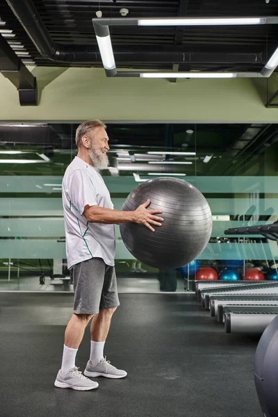 Fröhlicher älterer Mann mit Fitnessball im Fitnessstudio, Workout, Fitness und Sport, aktiver Lebensstil — Stockfoto
