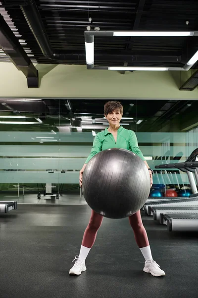 Mujer feliz haciendo ejercicio con la pelota de fitness en el gimnasio, senior activo, fitness y deporte, desgaste activo - foto de stock