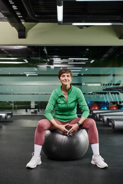 Mulher idosa feliz sentado na bola de fitness, olhando para a câmera após o treino, fitness e esporte — Fotografia de Stock