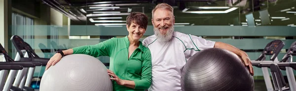 Sporty elderly couple, happy man and woman holding fitness balls, active seniors in gym, banner — Stock Photo