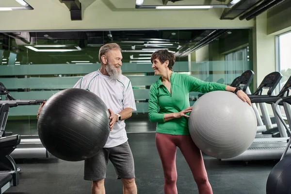 Пожилая пара, счастливый мужчина и женщина держат фитнес-мячи, активные пожилые смотрят друг на друга — стоковое фото