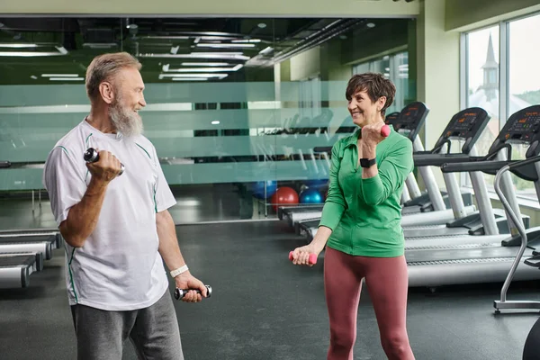 Pareja de ancianos, hombre y mujer alegres haciendo ejercicio con pesas, personas mayores activas mirándose - foto de stock