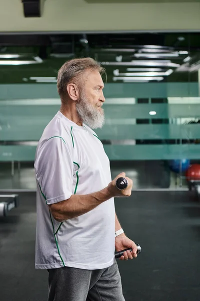 Вид сбоку босоногого пожилого человека, выполняющего упражнения с гантелями в тренажерном зале, активный пенсионер, фитнес-рутина — стоковое фото