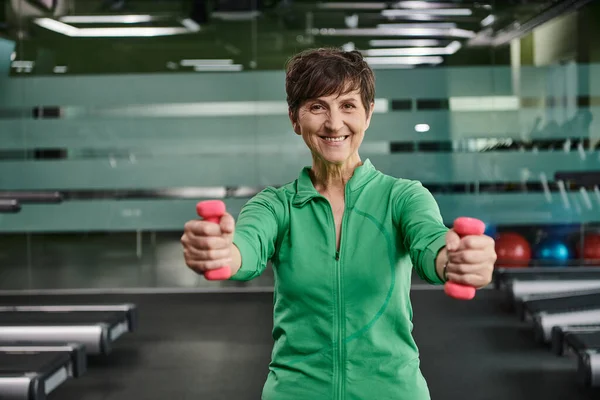 Happy woman with short hair working out with dumbbells, looking at camera in gym, portrait — Stock Photo