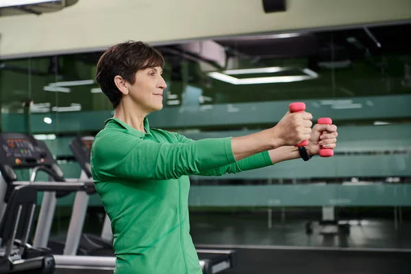 Mujer feliz con el pelo corto haciendo ejercicio con pesas en el gimnasio, senior activo, estilo de vida saludable - foto de stock