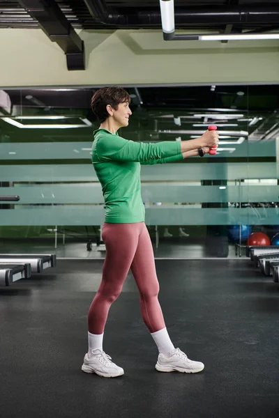 Ältere Frau, die im Fitnessstudio mit Kurzhanteln trainiert, aktive Kleidung, gesunder Lebensstil, volle Länge — Stockfoto