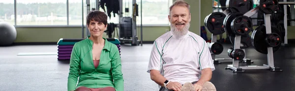 Heureux couple âgé assis et regardant la caméra dans la salle de gym, personnes âgées actives, mode de vie sain, bannière — Photo de stock