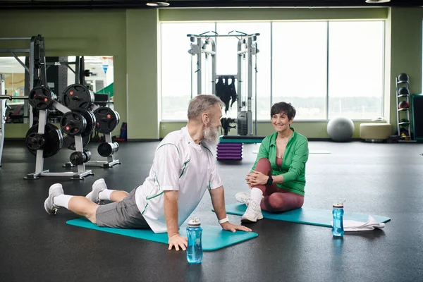 Elderly man stretching back near happy woman, fitness mats, active seniors, vibrant and healthy — Stock Photo