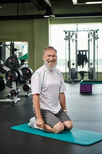 Glücklicher älterer Mann mit Bart auf Fitnessmatte sitzend, aktiver Senior, lebhaft und gesund, positiv — Stockfoto