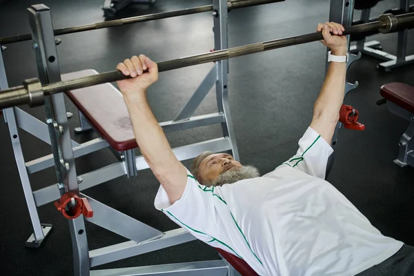 Fuerte anciano con barba haciendo ejercicio con barra en el gimnasio, senior activo, atleta, fuerza - foto de stock