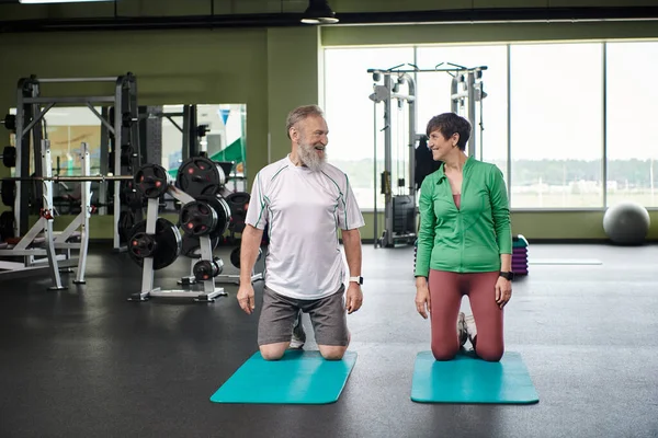 Happy senior couple, elderly man and woman looking at each other in gym, near fitness mats, active — Stock Photo