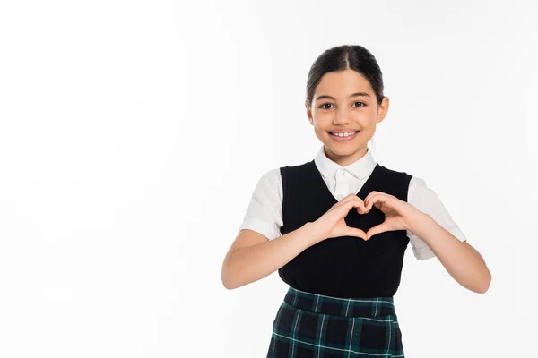 Glückliches Schulmädchen in schwarzer Weste, das Herzzeichen mit Händen zeigt und isoliert auf weiße Kamera blickt — Stockfoto