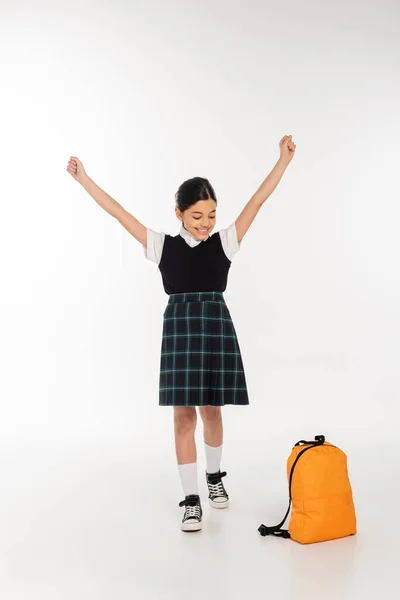 Fröhliches Mädchen, das auf den Rucksack blickt und mit ausgestreckten Händen dasteht, jawohl, zurück zum Schulkonzept — Stockfoto