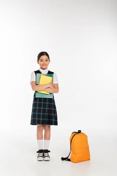 Счастливая школьница стоит с ноутбуками в руках рядом рюкзак, обратно в школу концепции, студент — стоковое фото