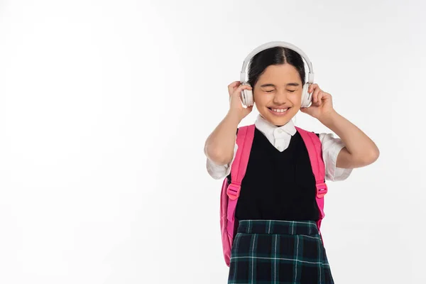 Joyous schoolgirl in wireless headphones listening music isolated on white background, closed eyes — Stock Photo