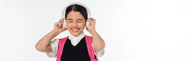 Joyous schoolgirl in wireless headphones listening music isolated on white, closed eyes, banner — Stock Photo