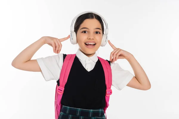 Збуджена школярка в бездротових навушниках слухає музику ізольовано на білому, дивлячись на камеру, радість — стокове фото