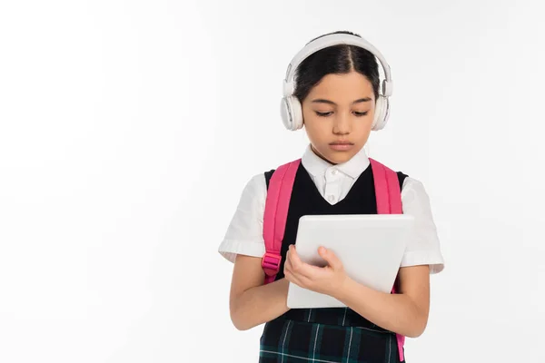 Сфокусированная школьница в беспроводных наушниках с помощью цифрового планшета, изолированного на белом, цифровом возрасте — стоковое фото