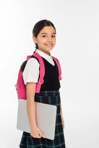 Scolaretta positiva che tiene il computer portatile e guarda la fotocamera, ragazza in uniforme scolastica, isolata sul bianco — Foto stock
