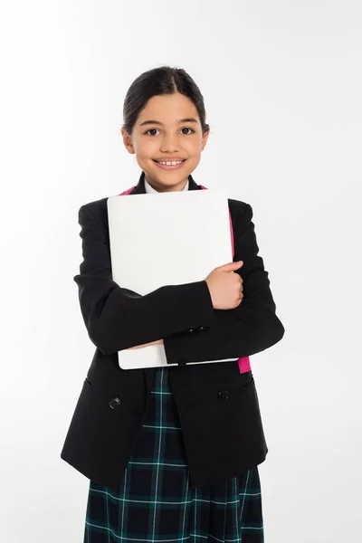 Joyeuse écolière tenant ordinateur portable et regardant caméra, fille en uniforme scolaire, isolé sur blanc — Photo de stock
