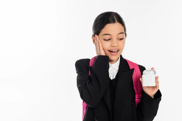 Amazed schoolgirl in uniform holding case with wireless earphones isolated on white, positive — Stock Photo