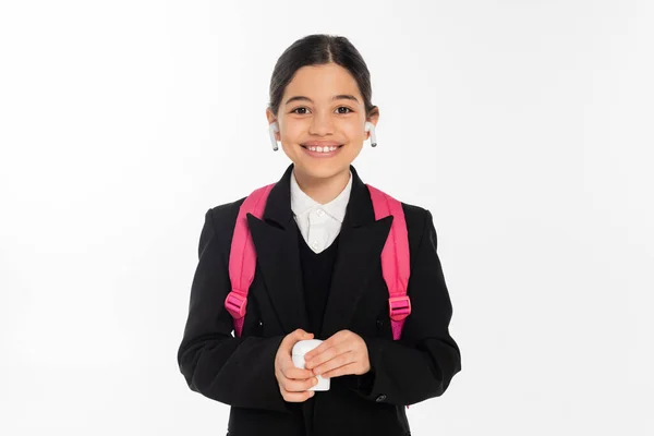 Estudante sorrindo em uniforme segurando caso e vestindo fones de ouvido sem fio isolados em branco, alegria — Fotografia de Stock