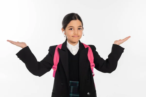Schoolgirl in uniform with wireless earphones in ears isolated on white, pointing with hands — Stock Photo