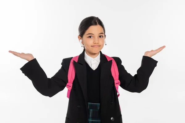 Écolière en uniforme avec écouteurs sans fil dans les oreilles isolées sur blanc, pointant avec les mains — Photo de stock