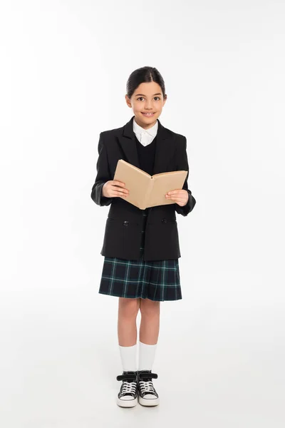 Felice studentessa in uniforme libro di lettura, studente bruna su sfondo bianco, lunghezza intera — Foto stock