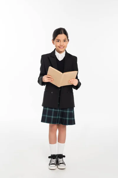 Aluna feliz no livro de leitura uniforme, estudante morena no fundo branco, comprimento total — Fotografia de Stock