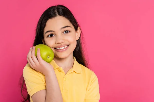 Retrato de chica morena feliz sosteniendo manzana verde y fresca aislado en rosa, vibrante telón de fondo - foto de stock