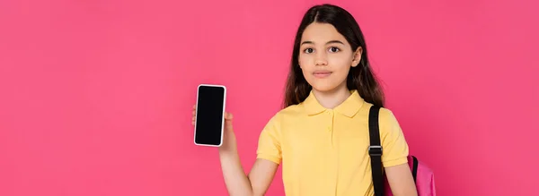 Brunette schoolgirl holding smartphone with blank screen and looking at camera on pink, banner — Stock Photo