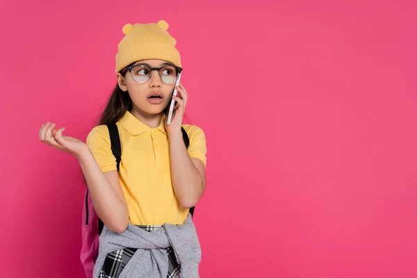 Schoolgirl in beanie hat and glasses talking smartphone on pink background, stylish look, phone call — Stock Photo