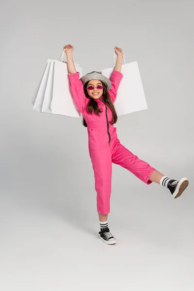 Весела дівчина в стильному рожевому вбранні і панамський капелюх тримає сумки на сірому фоні — стокове фото