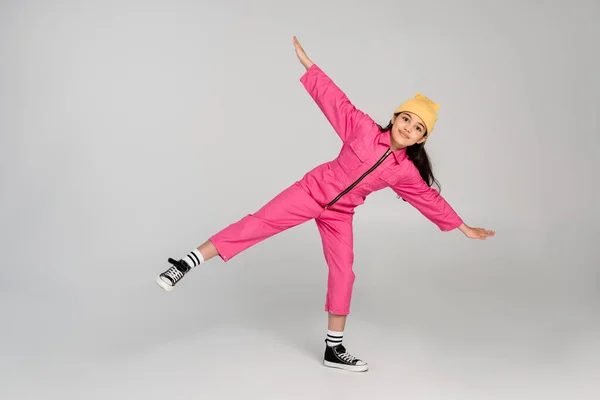 Happy girl in beanie hat and stylish pink outfit posing with outstretched hands on grey, have fun — Stock Photo