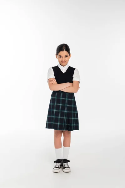 Full length, offended schoolkid in uniform looking at camera and standing with folded arms on white — Stock Photo