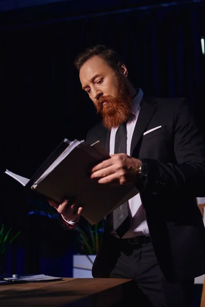 Бородатый бизнесмен в элегантной формальной одежде работает с документами в офисе ночью, вид под низким углом — стоковое фото