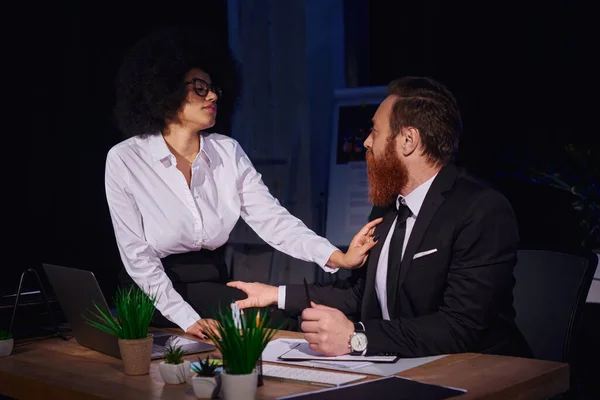 Afro-américaine femme d'affaires tentant homme barbu sur le lieu de travail, histoire d'amour dans le bureau de nuit — Photo de stock