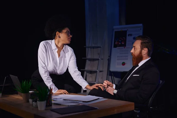 Charming african american woman sitting on work desk and touching bearded businessman, seduction — Stock Photo