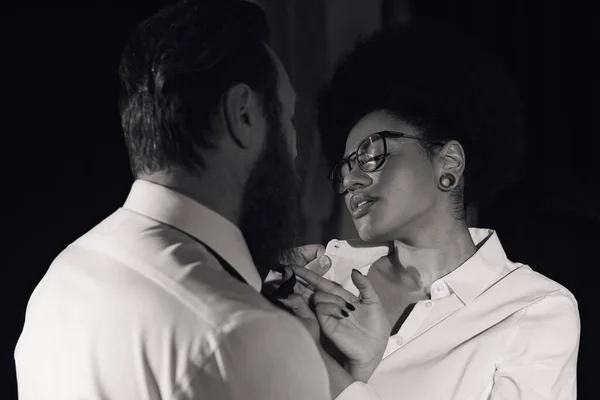 Foto monocromática de mujer afroamericana en anteojos seduciendo a hombre de negocios barbudo en la oficina - foto de stock