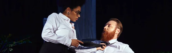 African american woman seducing bearded businessman and pulling his tie in night office, banner — Stock Photo