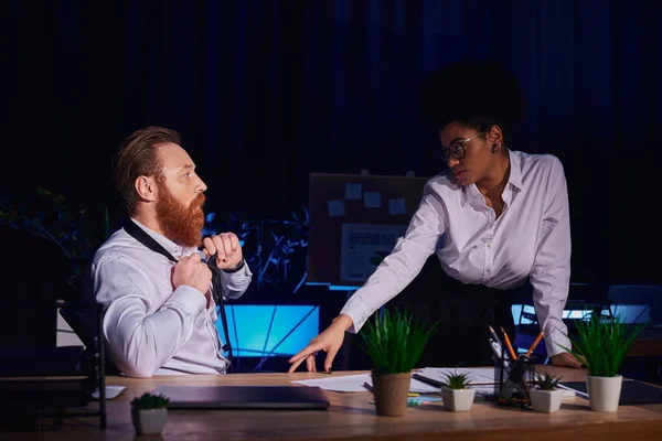 African american woman seducing bearded businessman undressing at workplace, romance in night office — Stock Photo