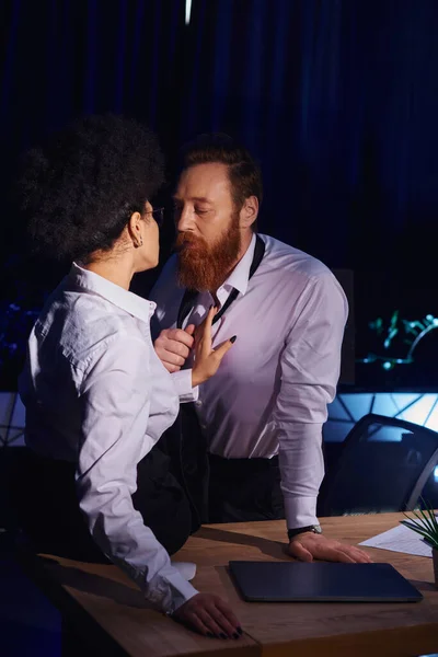 Charismatic bearded businessman undressing near young african american woman in office at night — Stock Photo