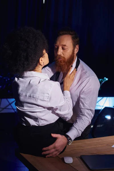 Young african american woman and bearded businessman hugging at night in office, romantic encounter — Stock Photo