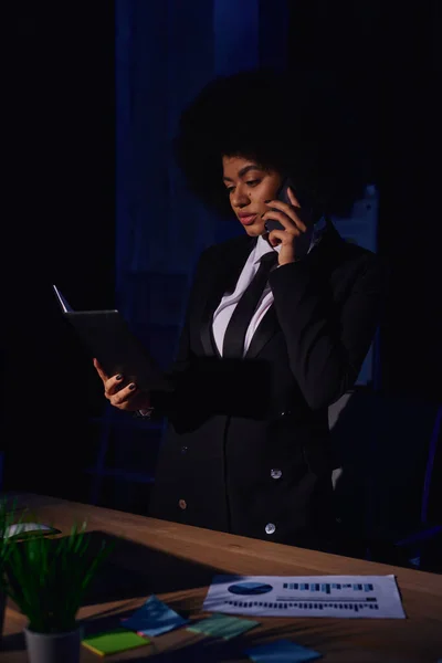 African american businesswoman with notebook talking on smartphone while working in office at night — Stock Photo