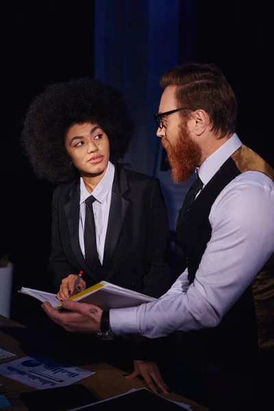 Interracial entrepreneurs looking at each other while working with documents at night in office — Stock Photo