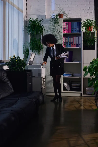 African american woman in stylish formal wear copying documents while working in office at night — Stock Photo